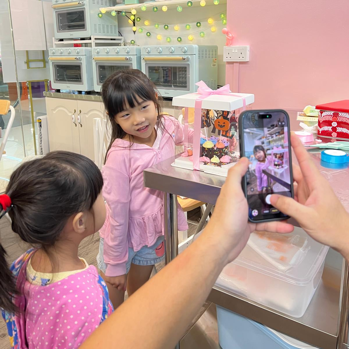 Two children in a toy store, one taking a photo of the other with a smartphone.