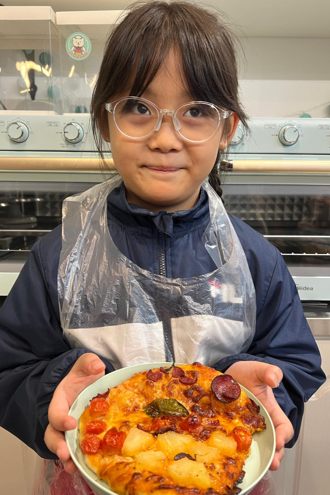 Child holding a homemade pizza in a kitchen