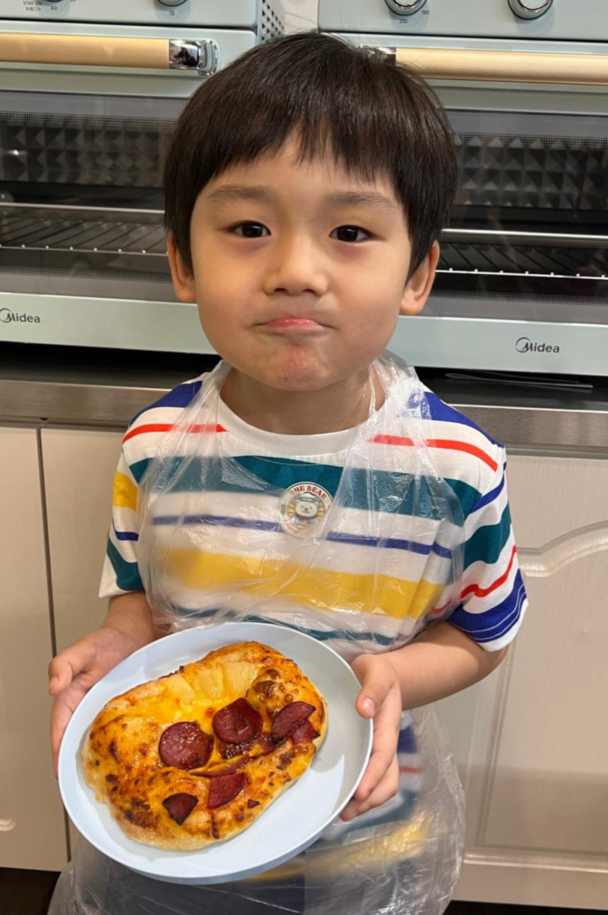 Child holding a small pizza in front of kitchen appliances