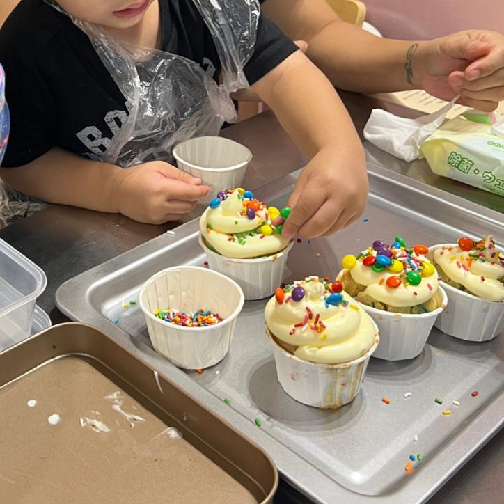 Children decorating cupcakes with colorful sprinkles in a kitchen setting.