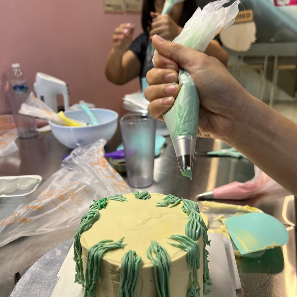 Person decorating a cake shaped like a pineapple with green icing.