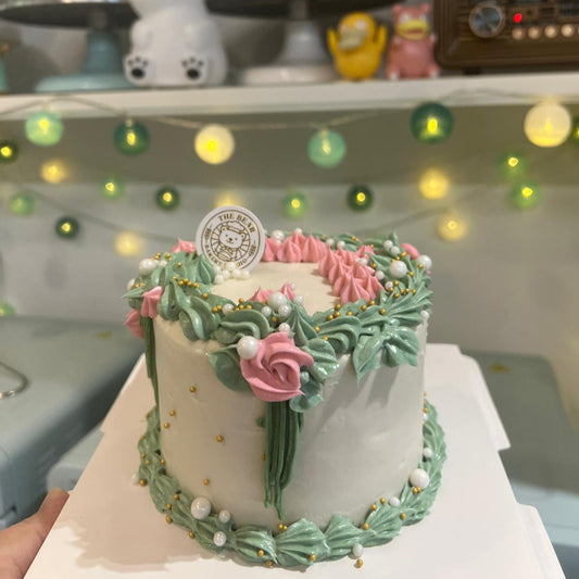 Decorative cake with pink and green icing on a white surface, with a shelf in the background featuring various items.