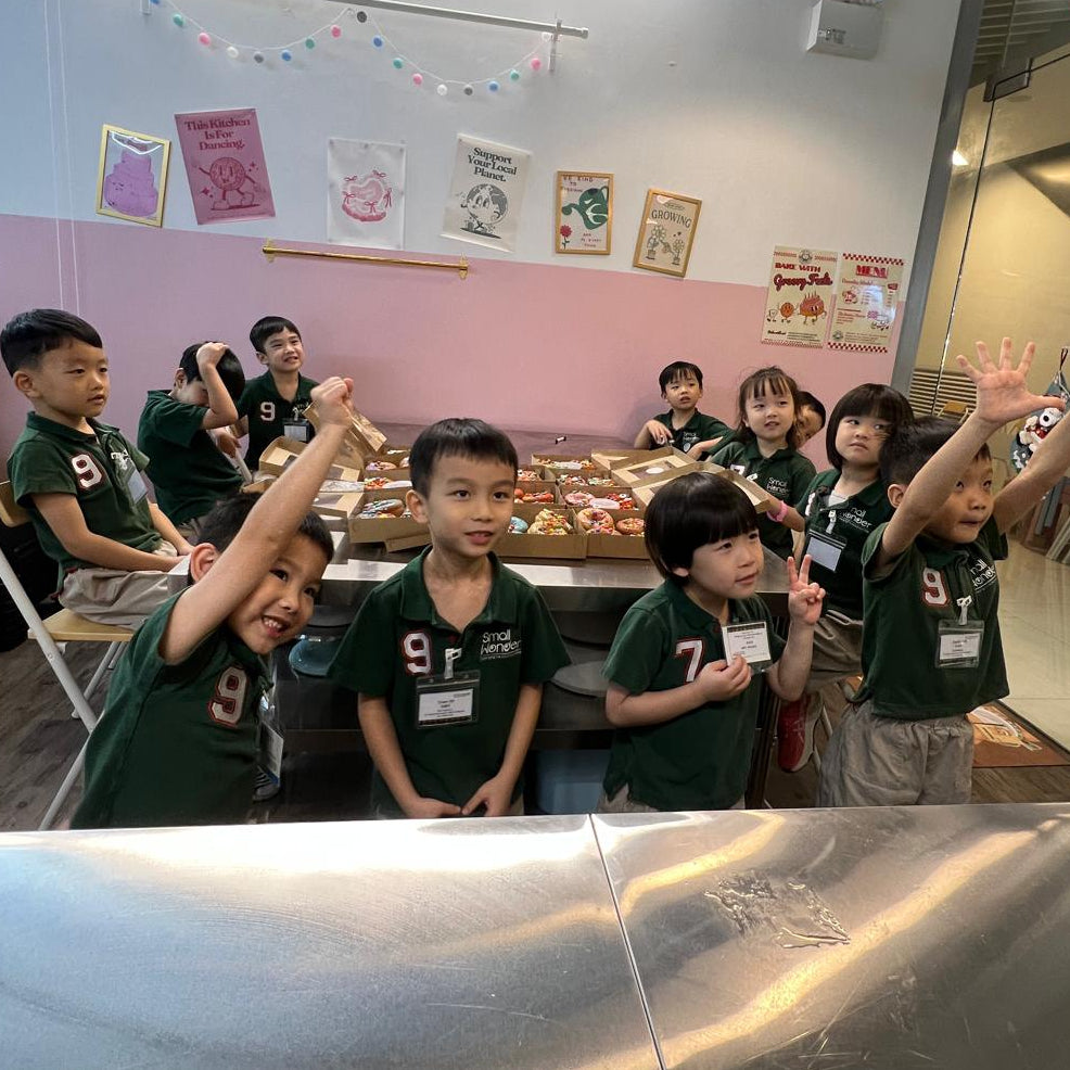 Children in green uniforms posing for a photo in a baking class setting.